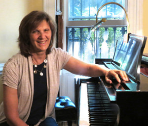 Fiona Bicket with a big smile sitting at a grand piano.